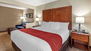 A hotel room with a large bed, a wooden headboard, a nightstand with a lamp, a chair, and a desk with a phone. - Comfort Inn & Suites Middletown - Franklin (Franklin)