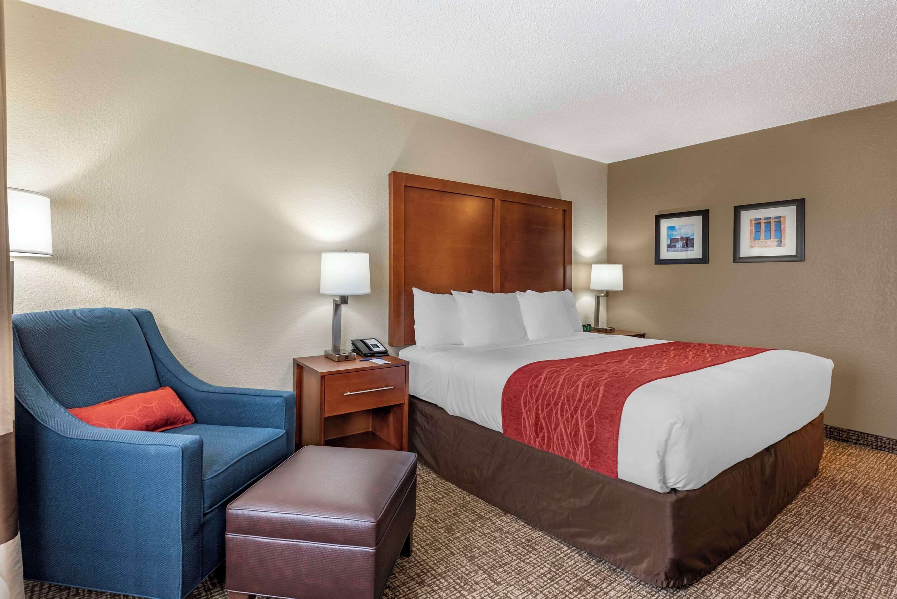 A hotel room with a bed, a blue armchair, a wooden nightstand, and two wall-mounted lamps.