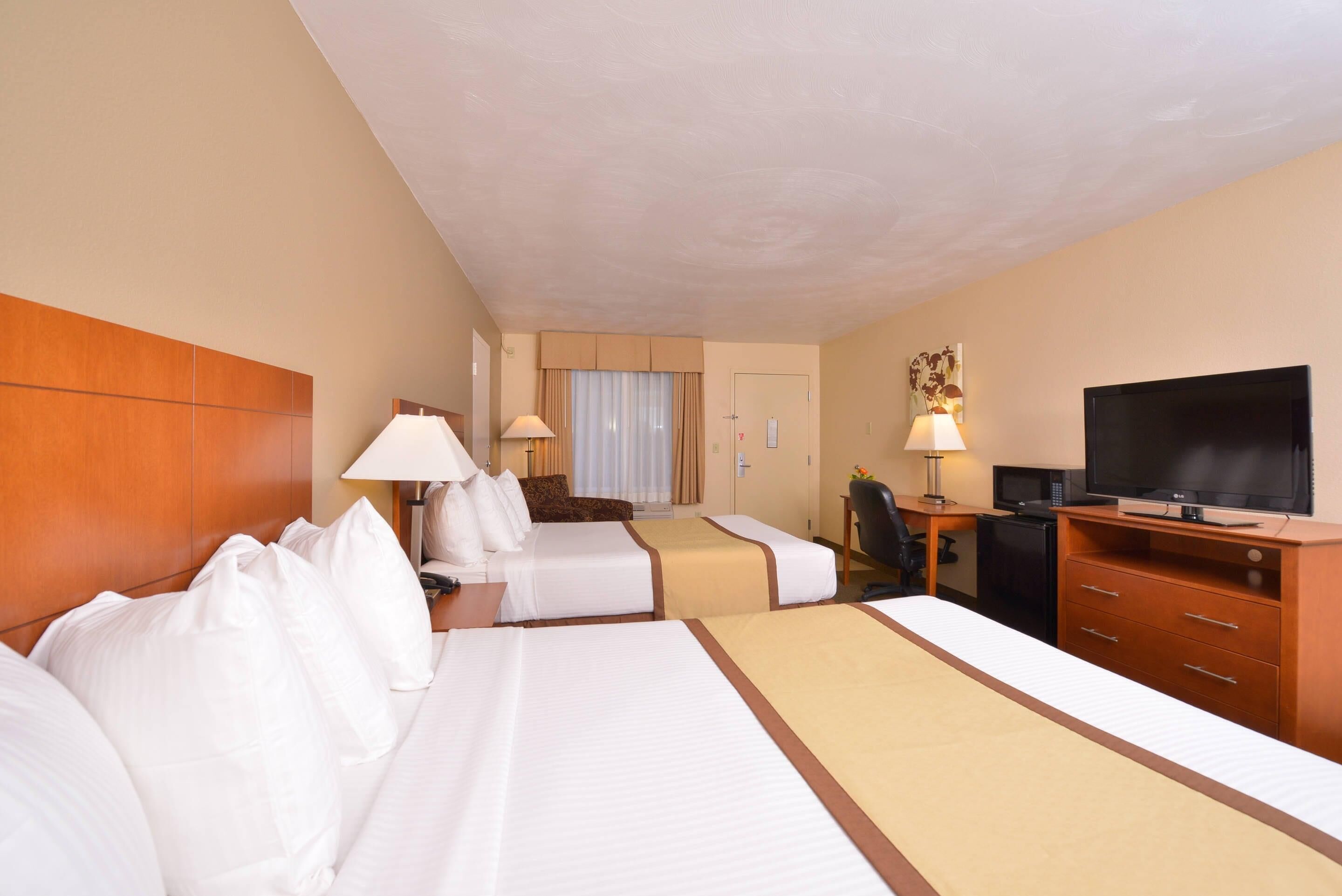 A hotel room with two beds, a desk with a computer, a television, and a minibar.