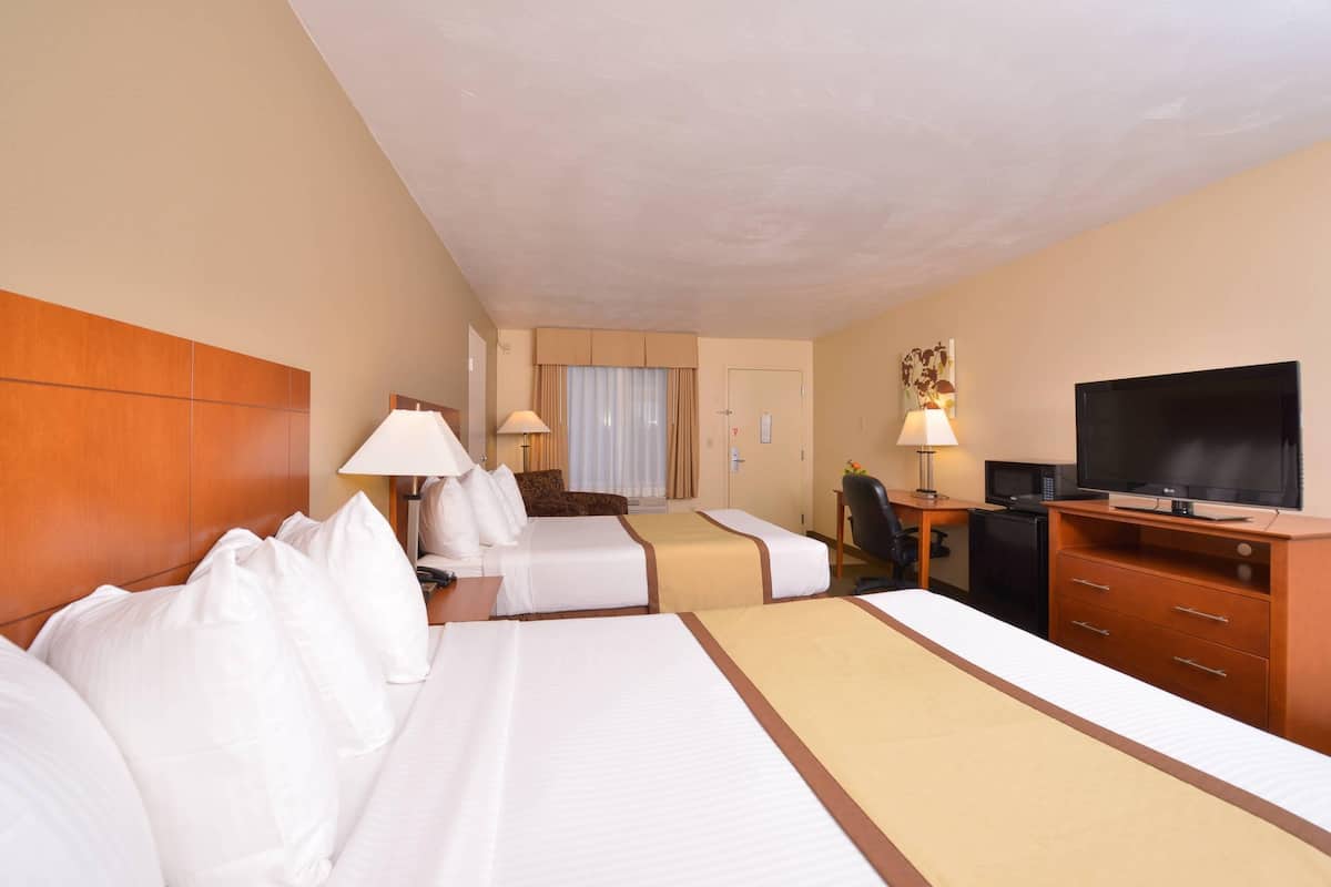 A hotel room with two beds, a desk with a computer, a television, and a minibar.