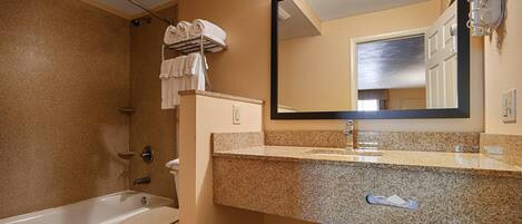 A bathroom with a bathtub, toilet, and a large mirror above a granite countertop.