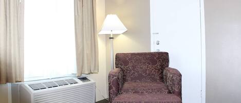 Una habitación con ventana, cortinas, lámpara de pie, una silla y un aire acondicionado.