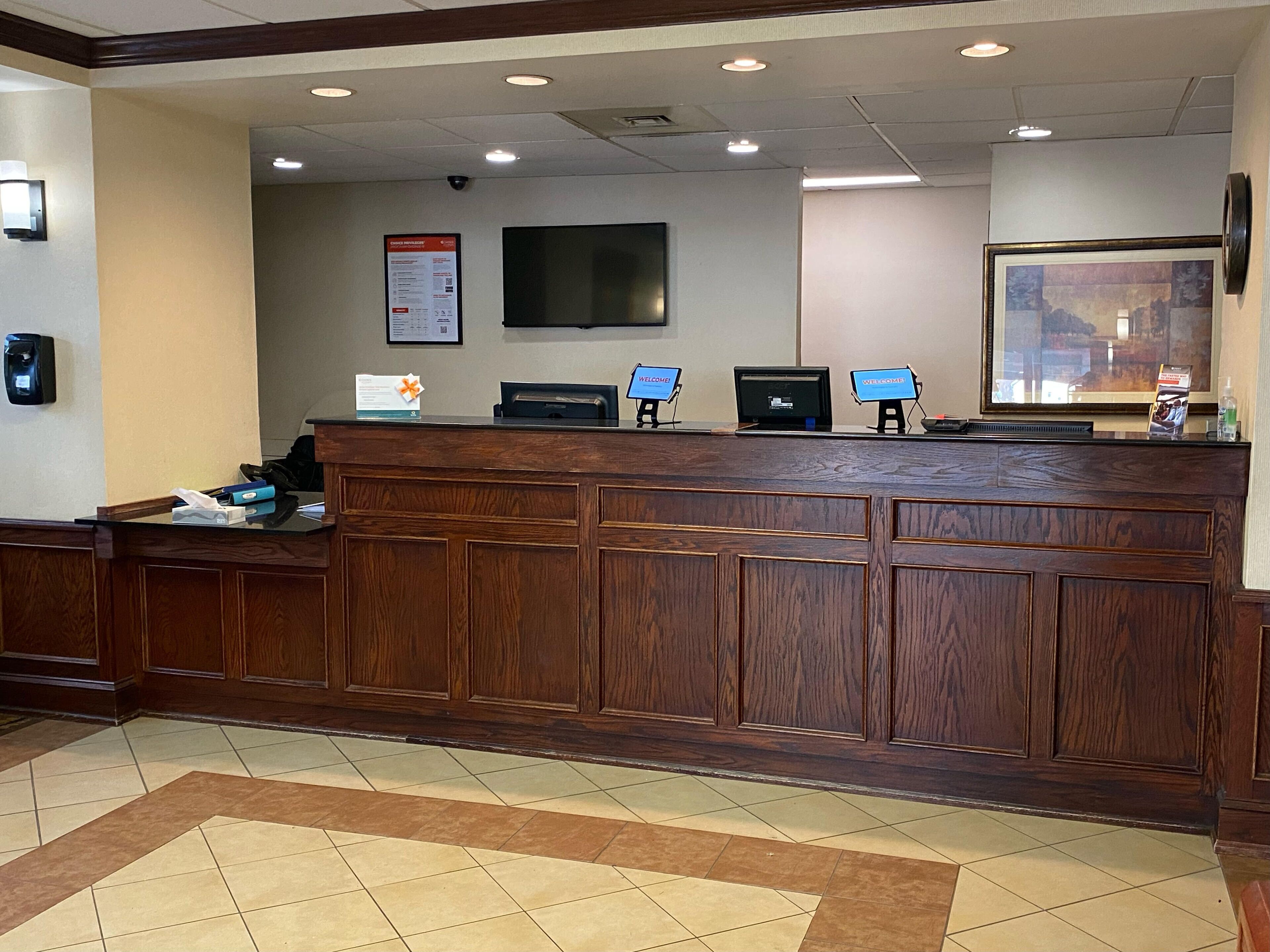 A reception desk with a wooden finish, a flat-screen TV mounted on the wall, and a framed picture above the desk.