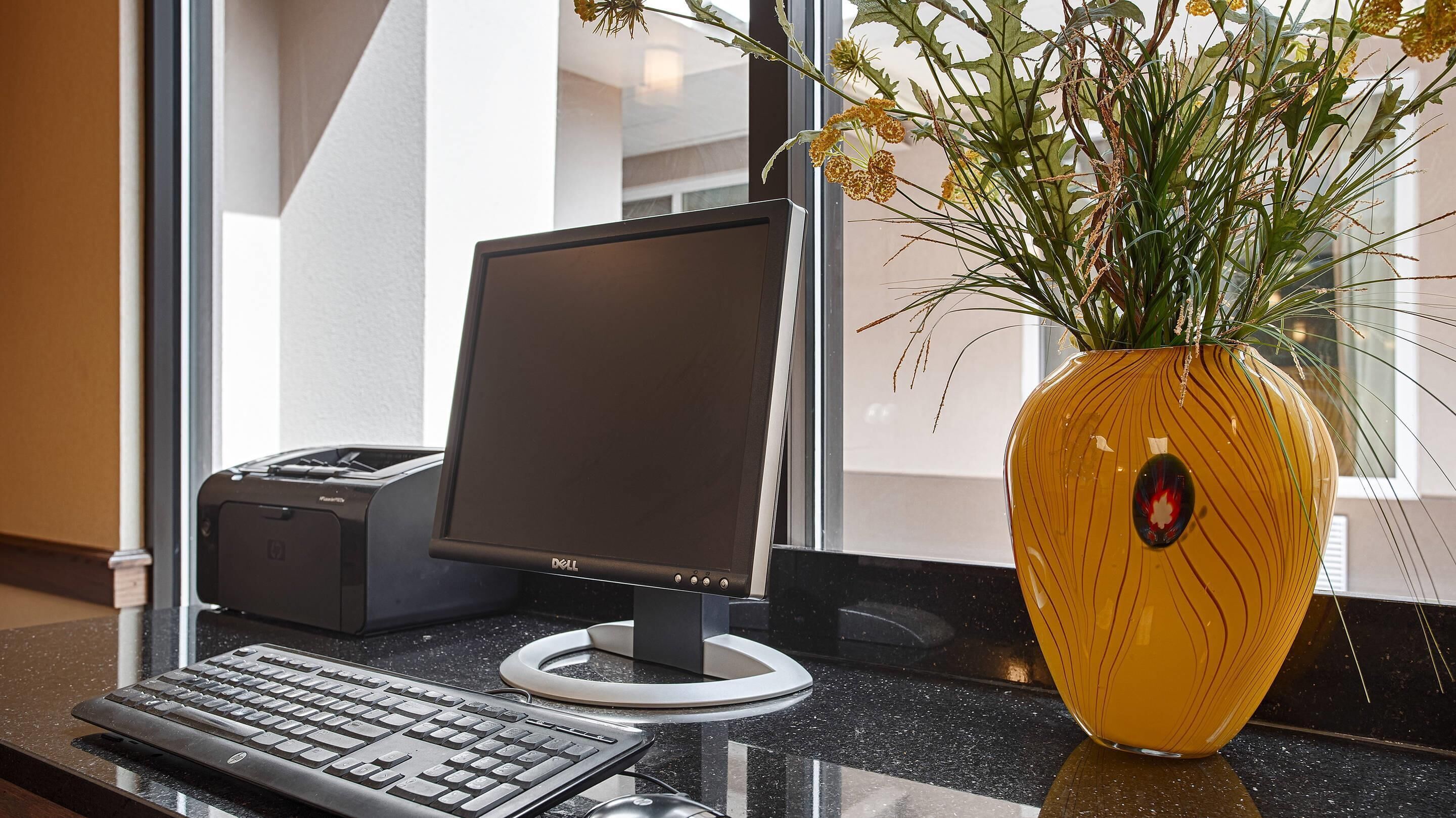 A desktop computer with a keyboard and mouse on a counter, a printer, and a vase with flowers.