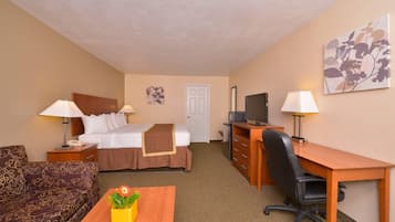 A hotel room with a bed, desk, chair, and a small table with a plant.