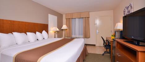 Habitación de hotel con una cama grande, televisor, escritorio con silla y ventana con cortinas.