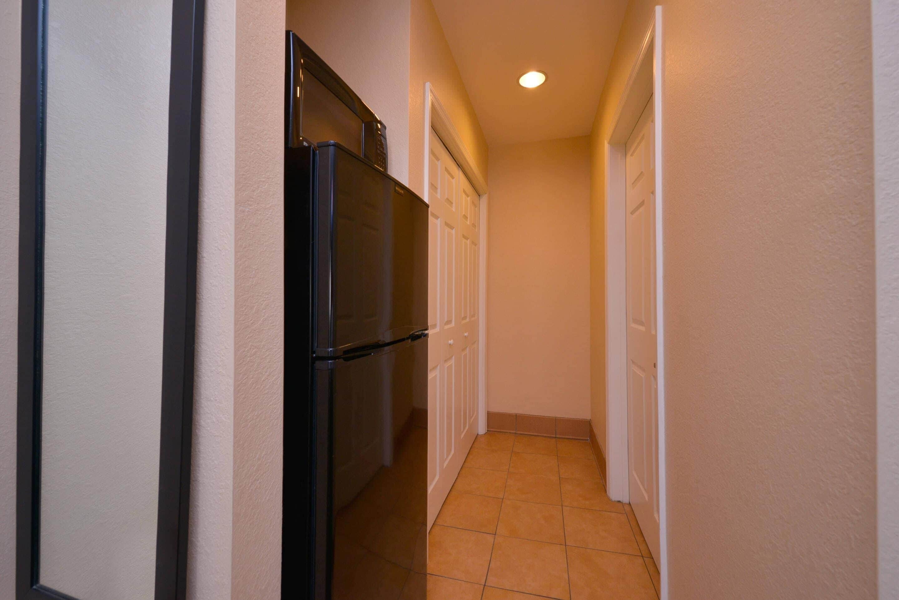 A narrow hallway with a refrigerator and cabinets, a door at the end, and a tiled floor.