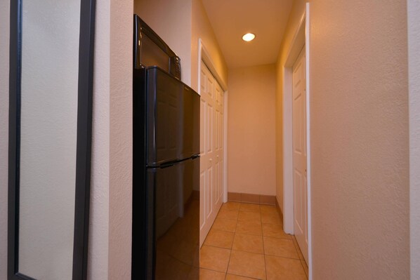 A narrow hallway with a refrigerator and cabinets, a door at the end, and a tiled floor.