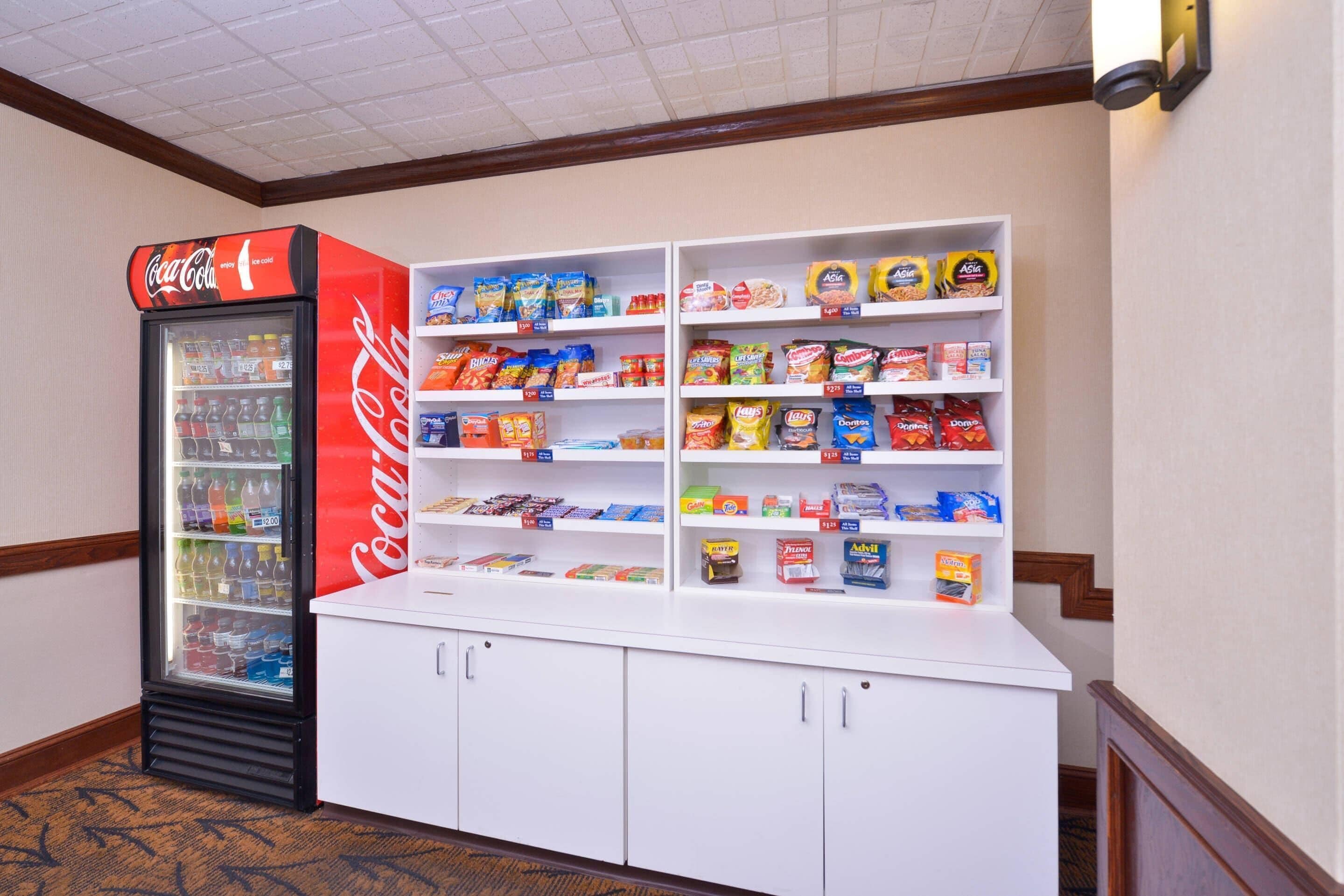 A vending machine stocked with beverages and snacks, and a white counter with shelves of various packaged goods.