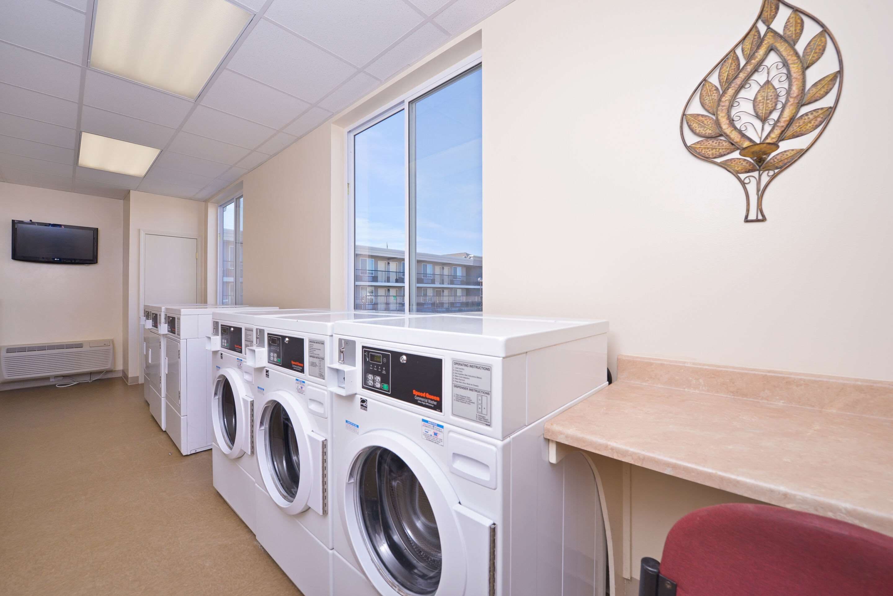 A laundry room with multiple washing machines, a large window, and a decorative wall piece.