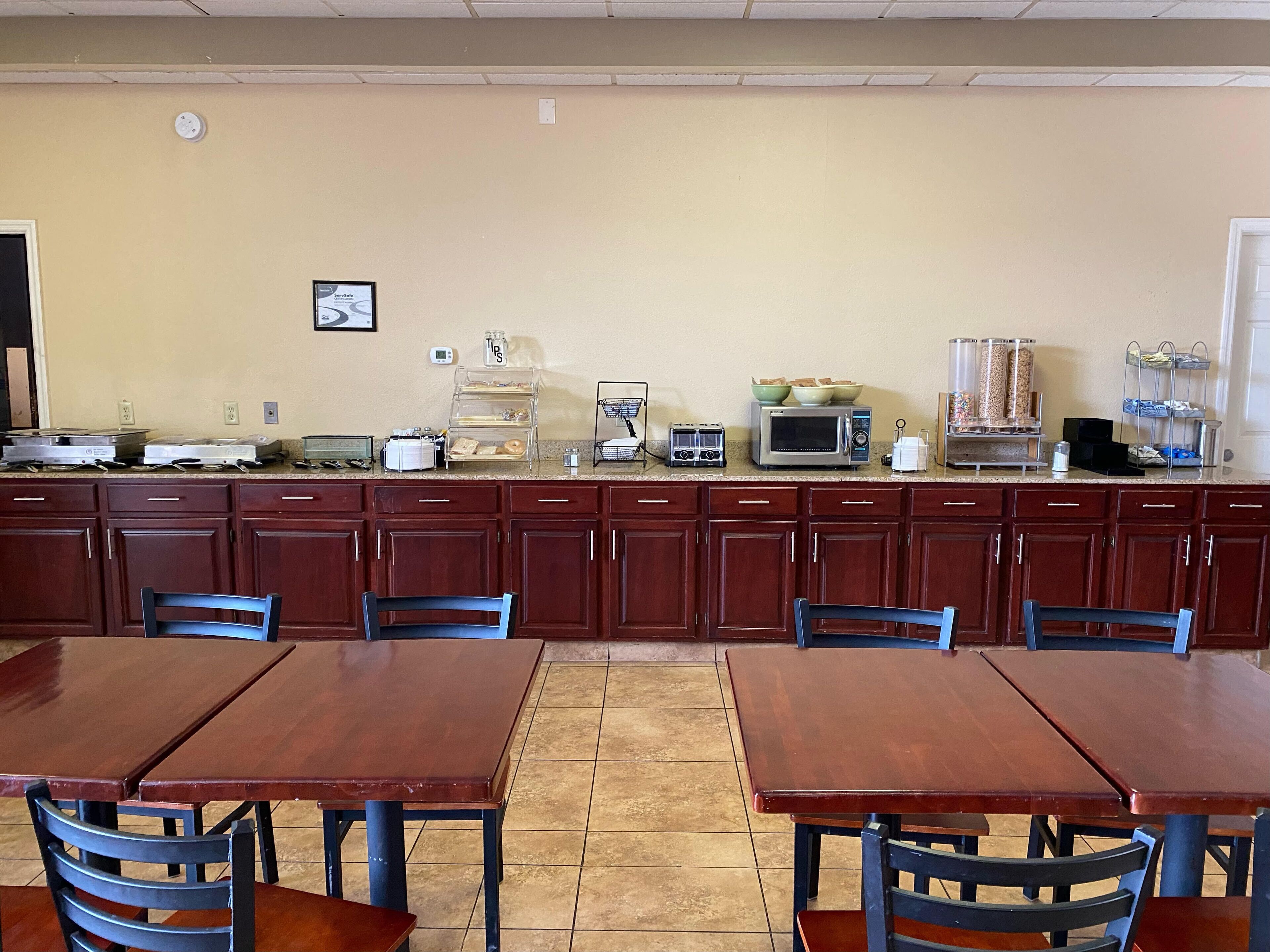 A kitchen with wooden cabinets, a microwave, and a coffee maker. There are tables and chairs for dining.