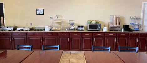 A kitchen with wooden cabinets, a microwave, and a coffee maker. There are tables and chairs for dining.