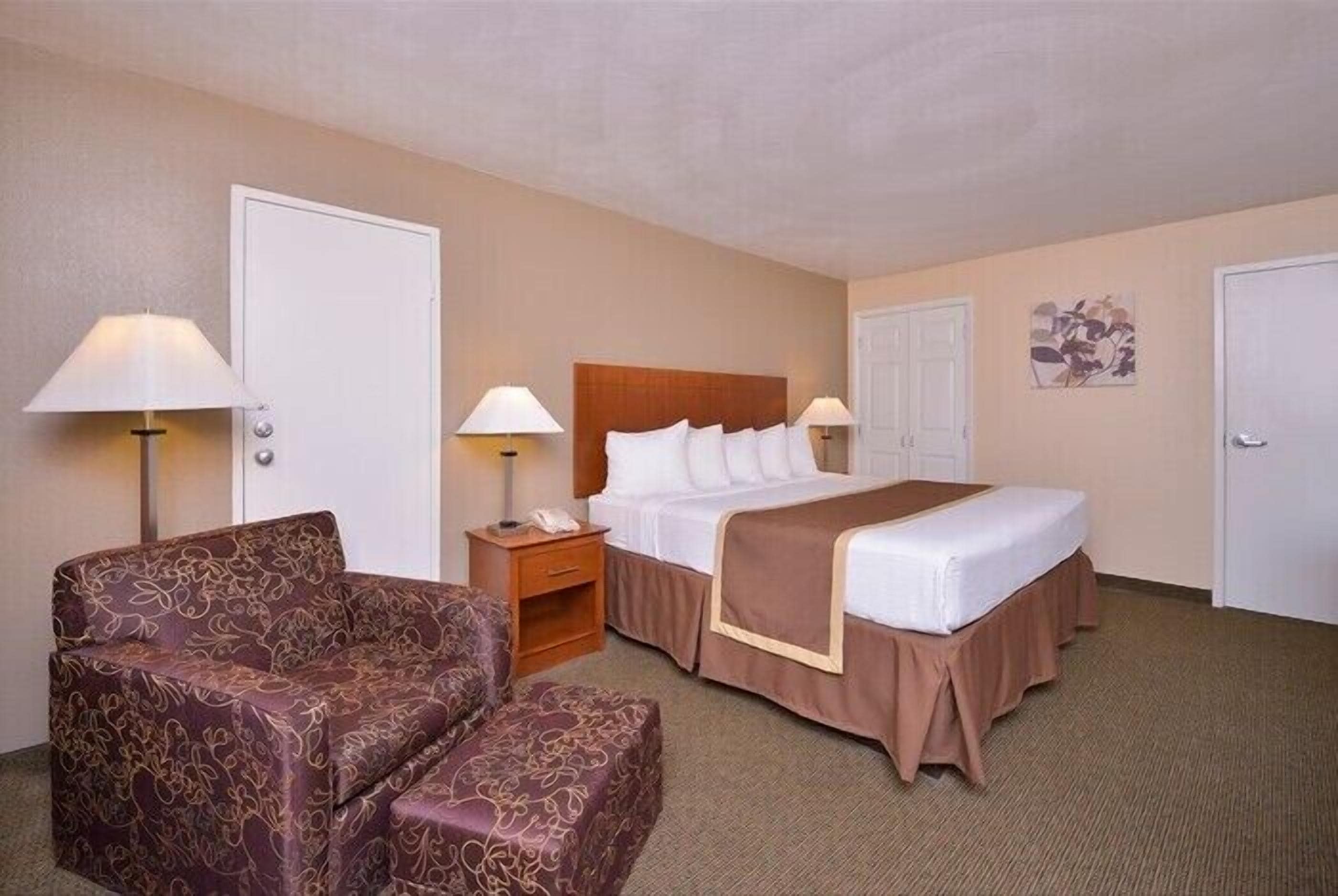 Una habitación de hotel con una cama, dos mesitas de noche, una lámpara, un sofá y una silla.