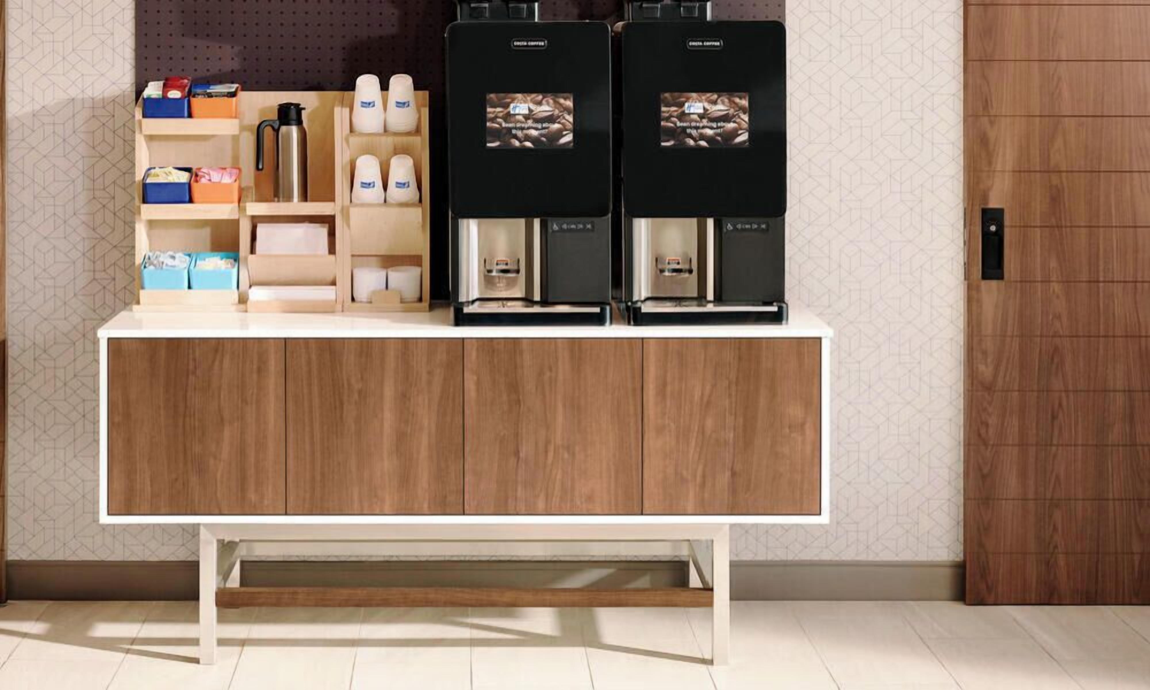A coffee station with two coffee machines and a shelf with coffee cups and a thermos.