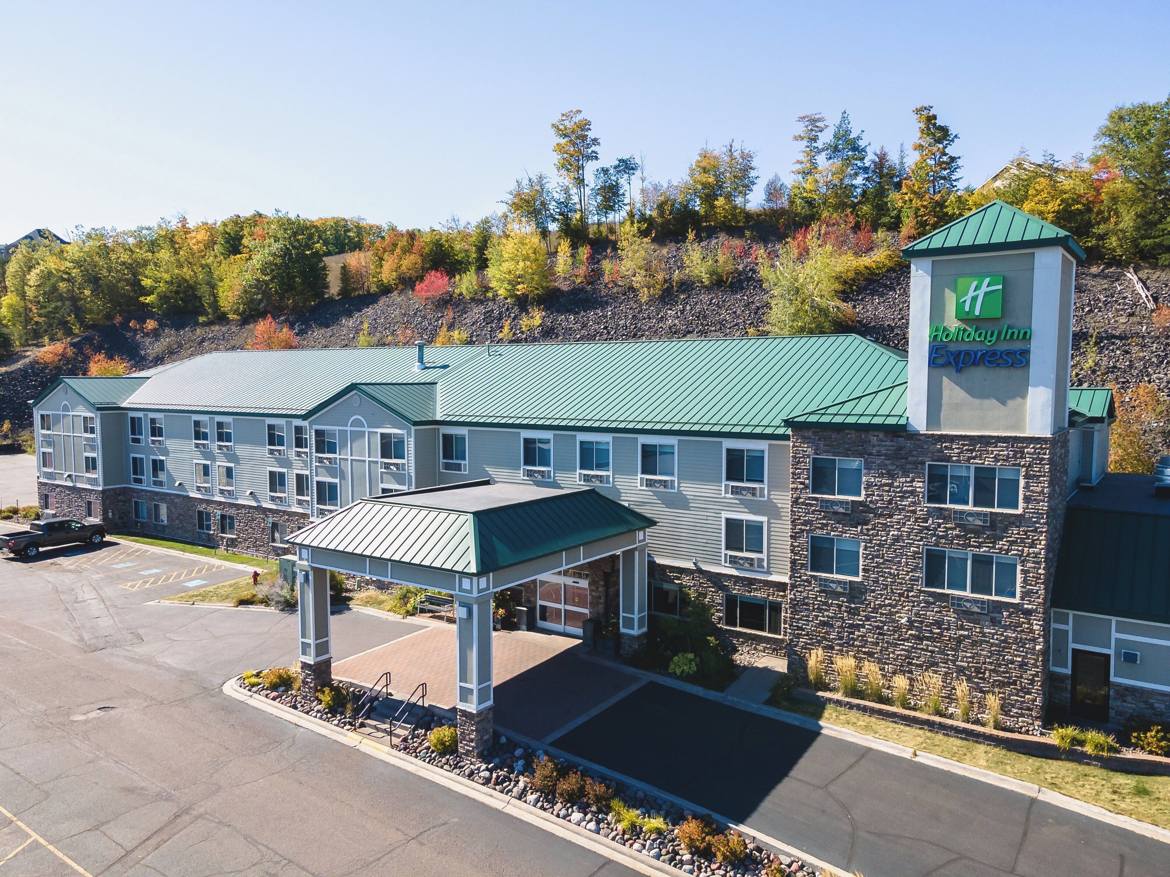 Un hotel Holiday Inn Express con fachada de piedra, techo verde y zona de estacionamiento cubierta.
