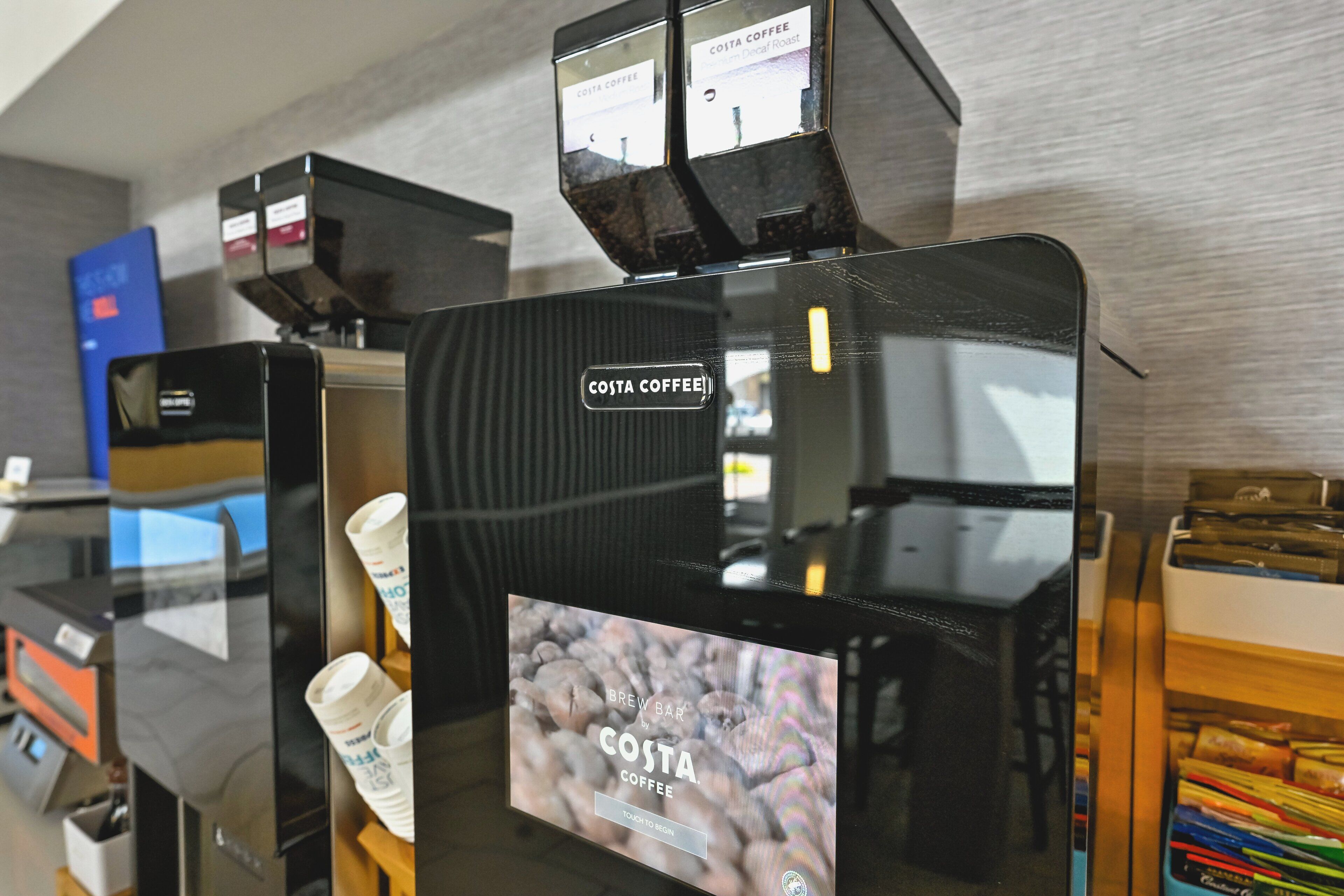 A coffee machine with a display screen advertising Costa Coffee.