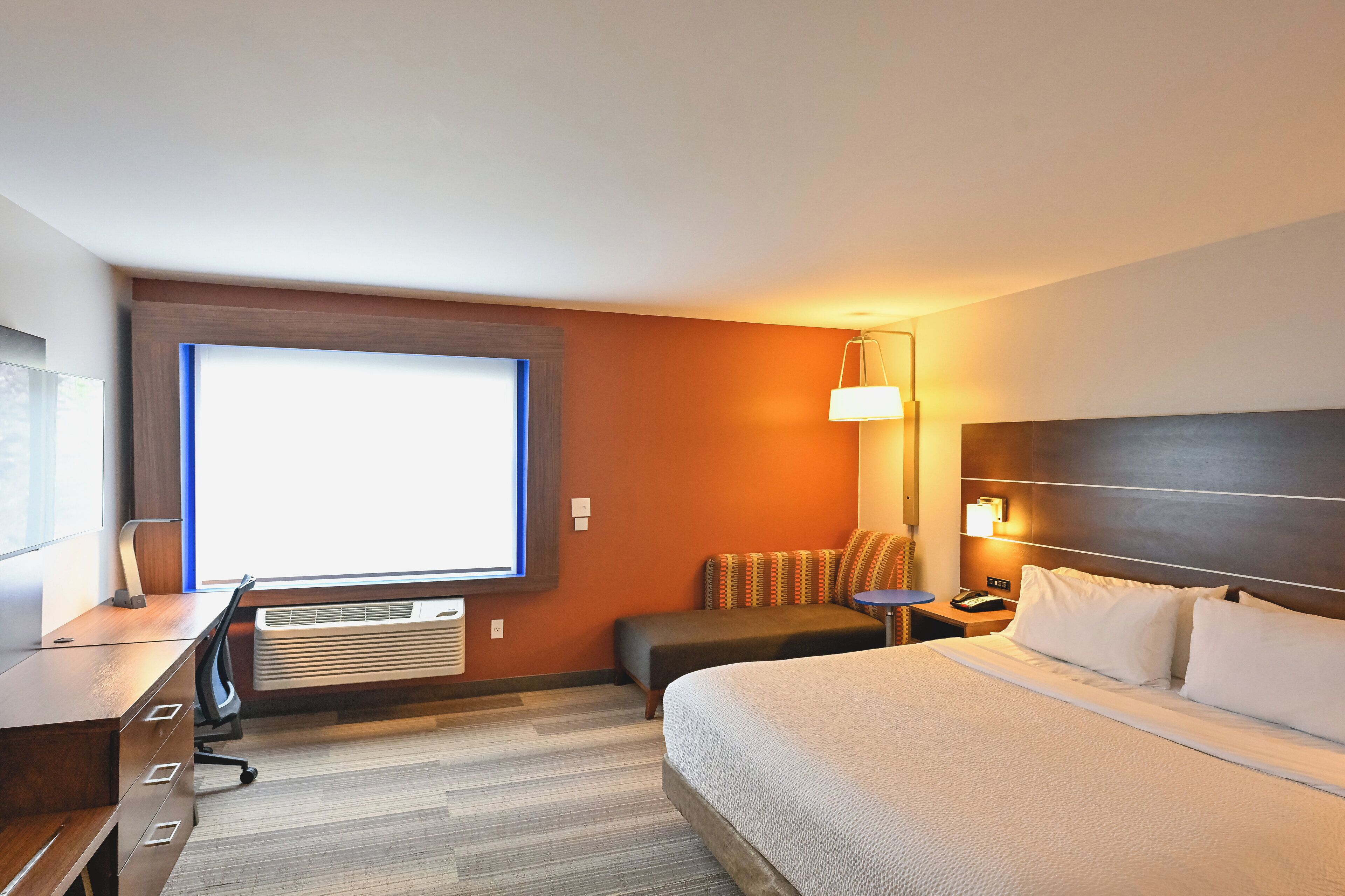 Une chambre d’hôtel avec un lit, un bureau, une chaise et une grande fenêtre.