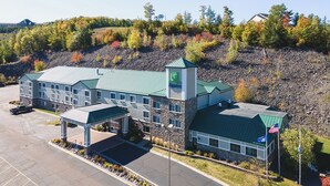 A Holiday Inn Express hotel with a green roof, a parking lot, and a mountainous backdrop. - Holiday Inn Express Houghton-Keweenaw by IHG (Houghton)