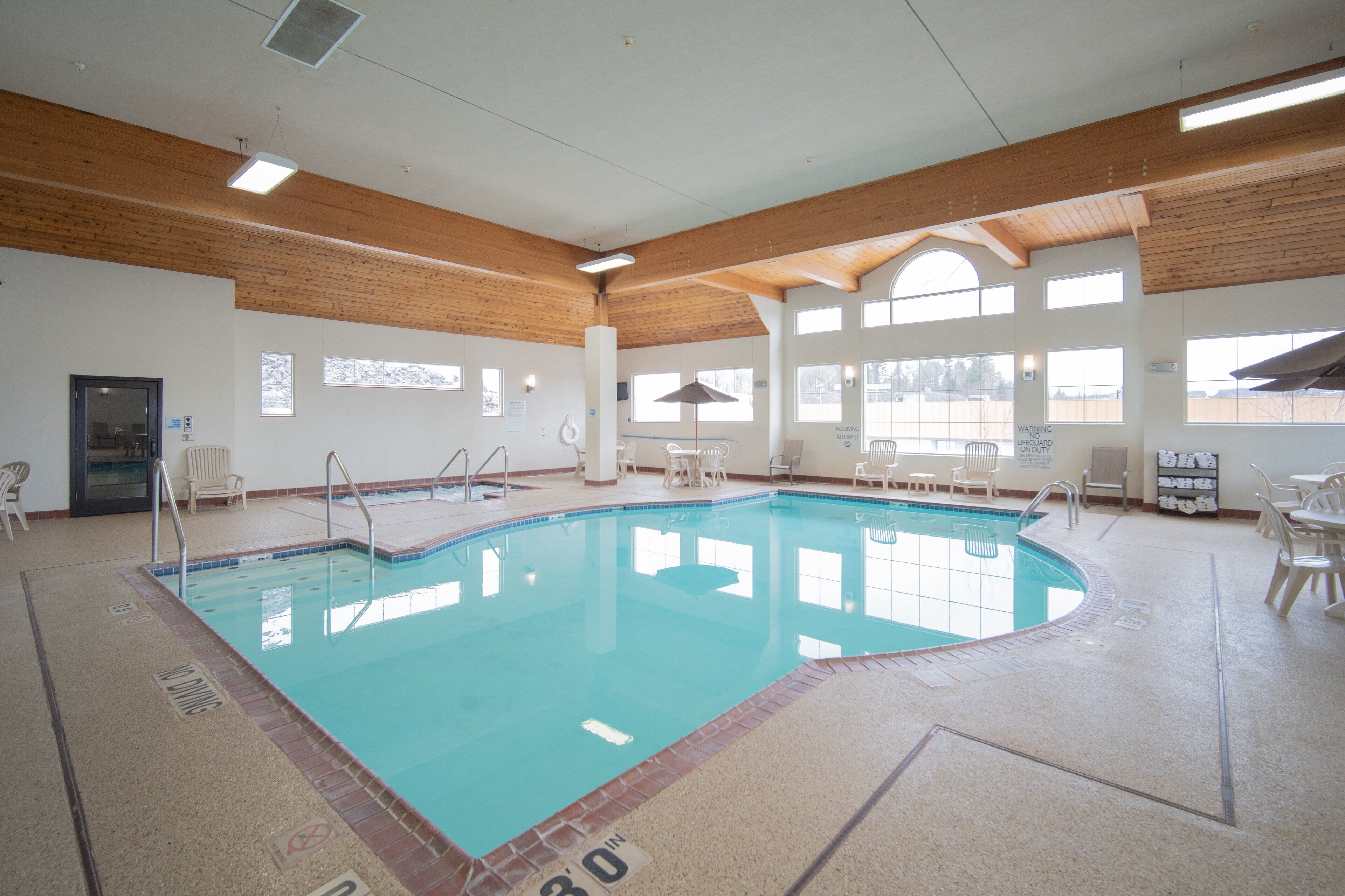 Una piscina interna con acqua cristallina, travi in legno al soffitto e diverse sedie intorno alla zona della piscina.