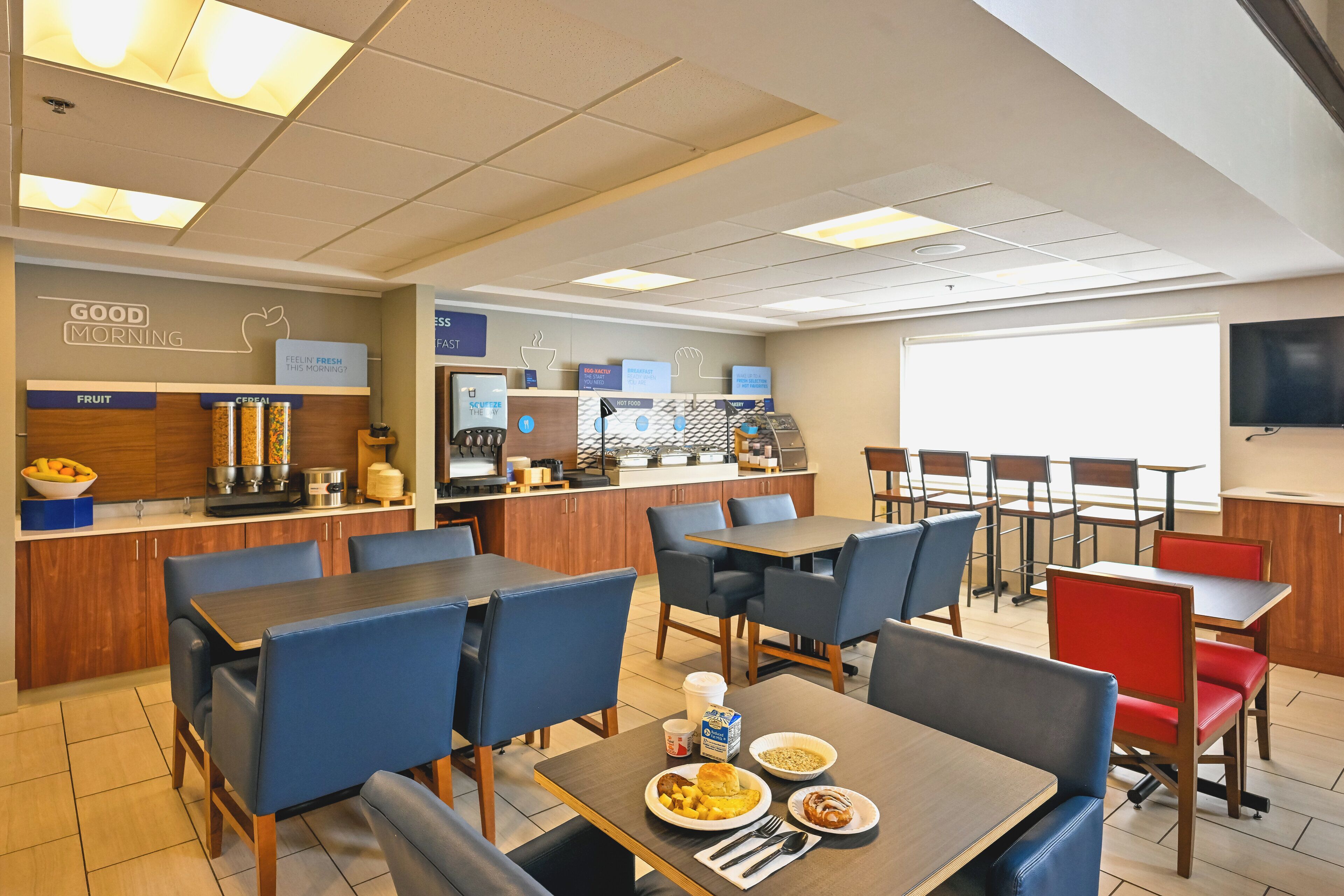 Ein Frühstücksbereich eines Hotels mit Tischen, Stühlen und einer Theke mit Speisen.