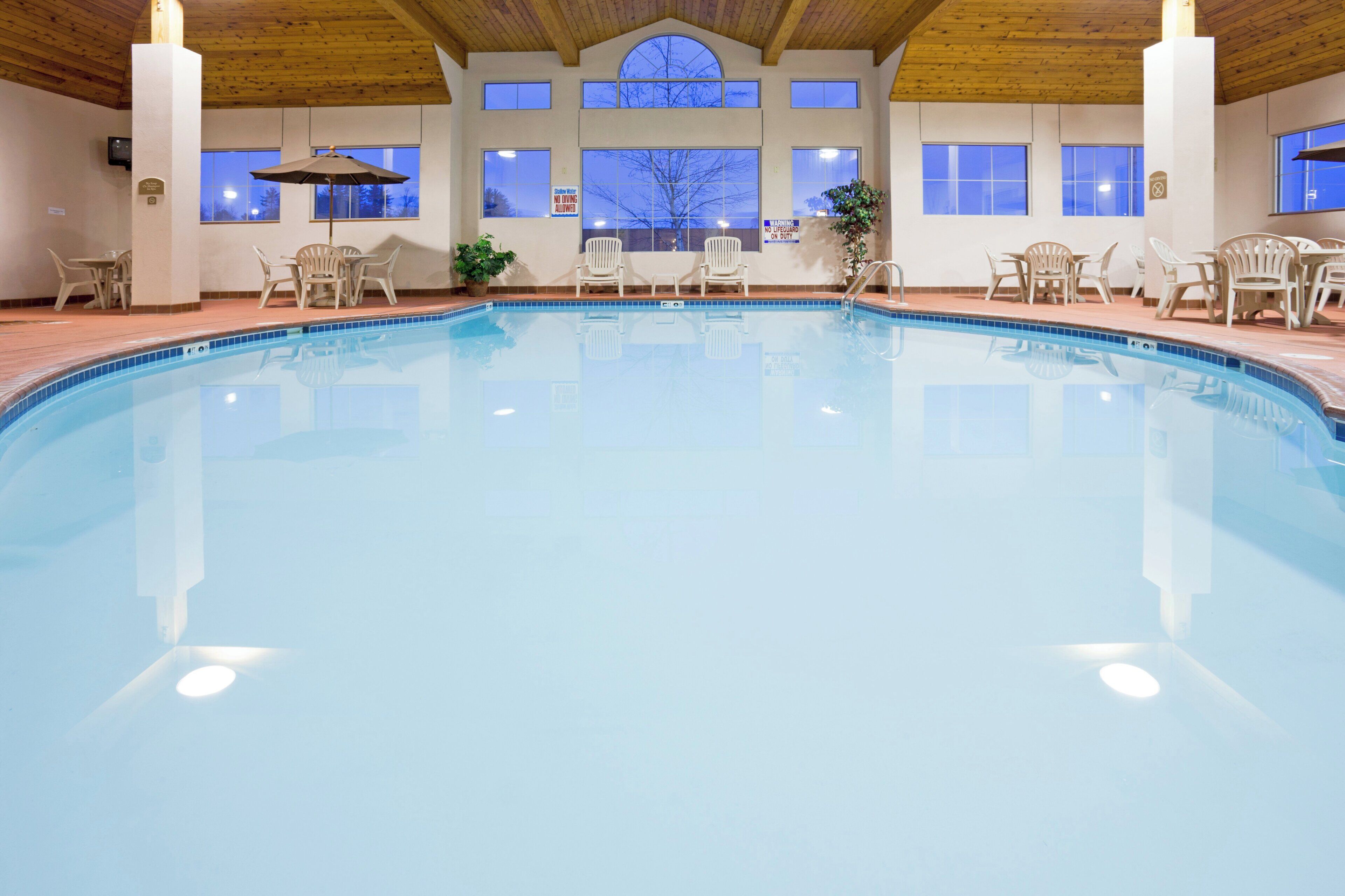 Ein Innenpool mit klarem, blauem Wasser, umgeben von weißen Stühlen und Tischen, mit einer Holzbalkendecke.
