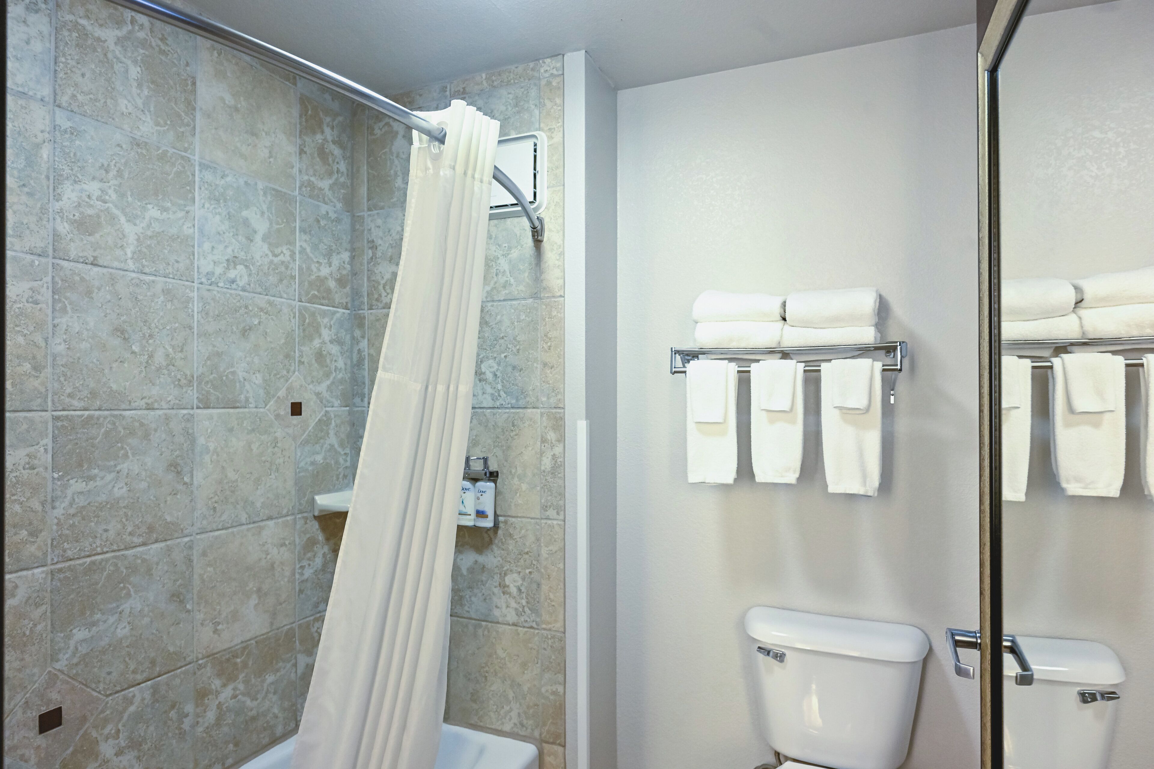 A bathroom with a shower, a toilet, and a towel rack with multiple towels.