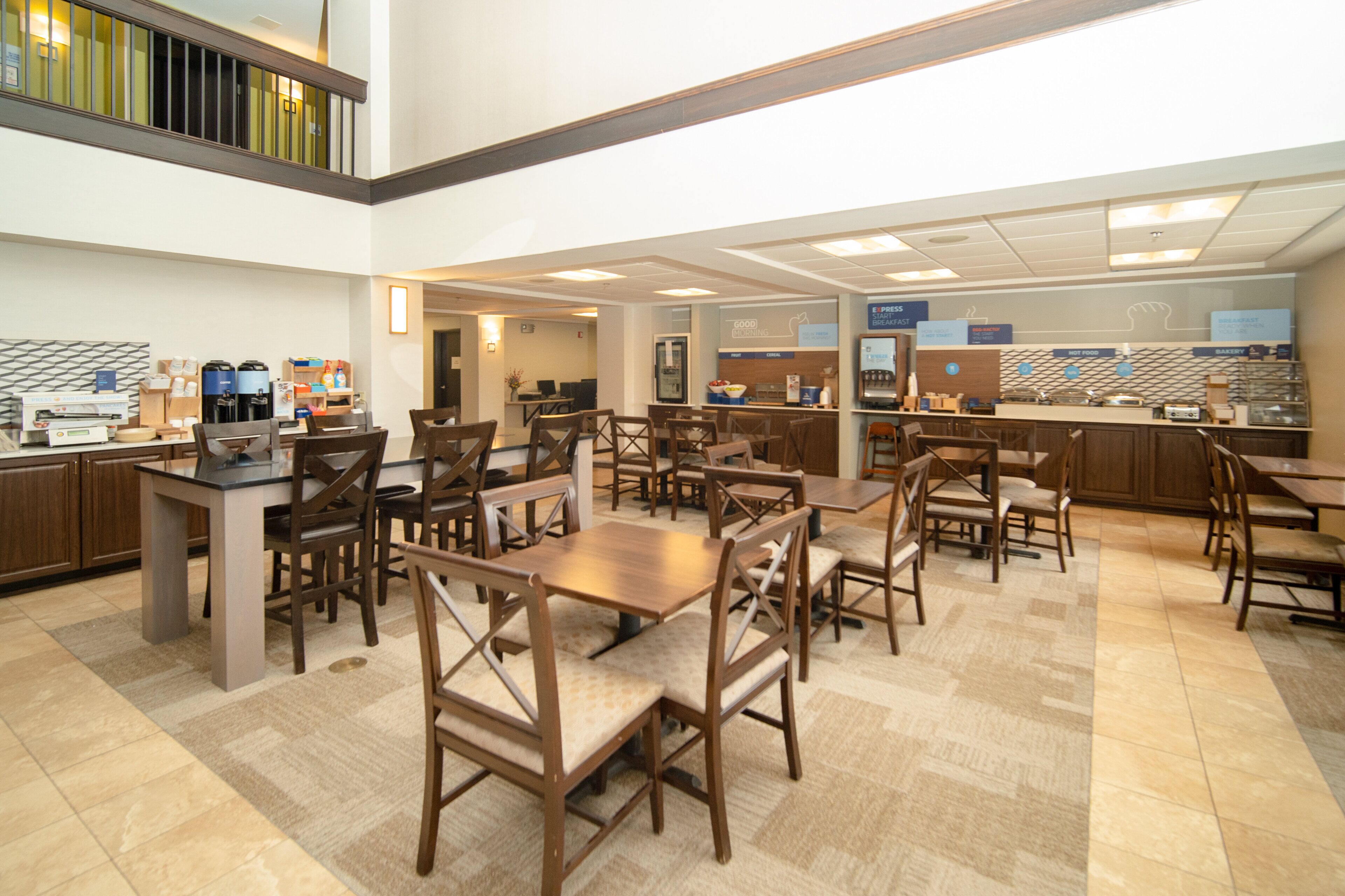 A spacious cafeteria with multiple dining tables and chairs, a coffee station, and a breakfast bar.
