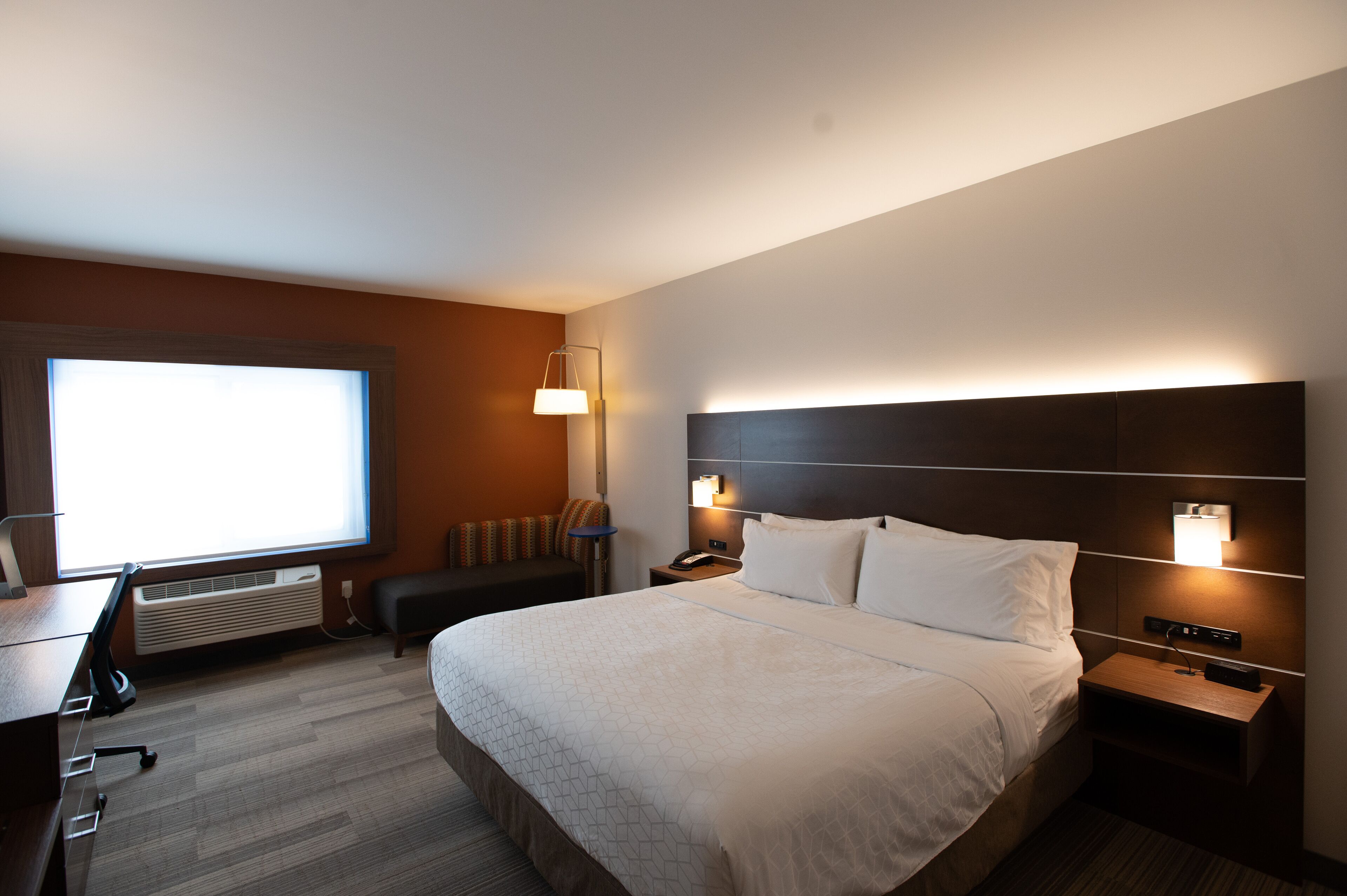 Ein Hotelzimmer mit einem großen Bett, einem Schreibtisch, einem Stuhl, einem Fernseher und einer Heizung.