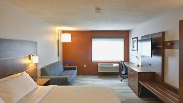 A hotel room with a bed, a sofa, a desk, a TV, and a window.