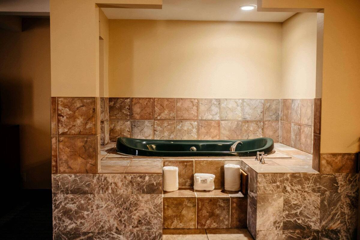 Um quarto de spa com uma grande banheira verde, paredes de mármore e um armário com artigos de higiene pessoal.
