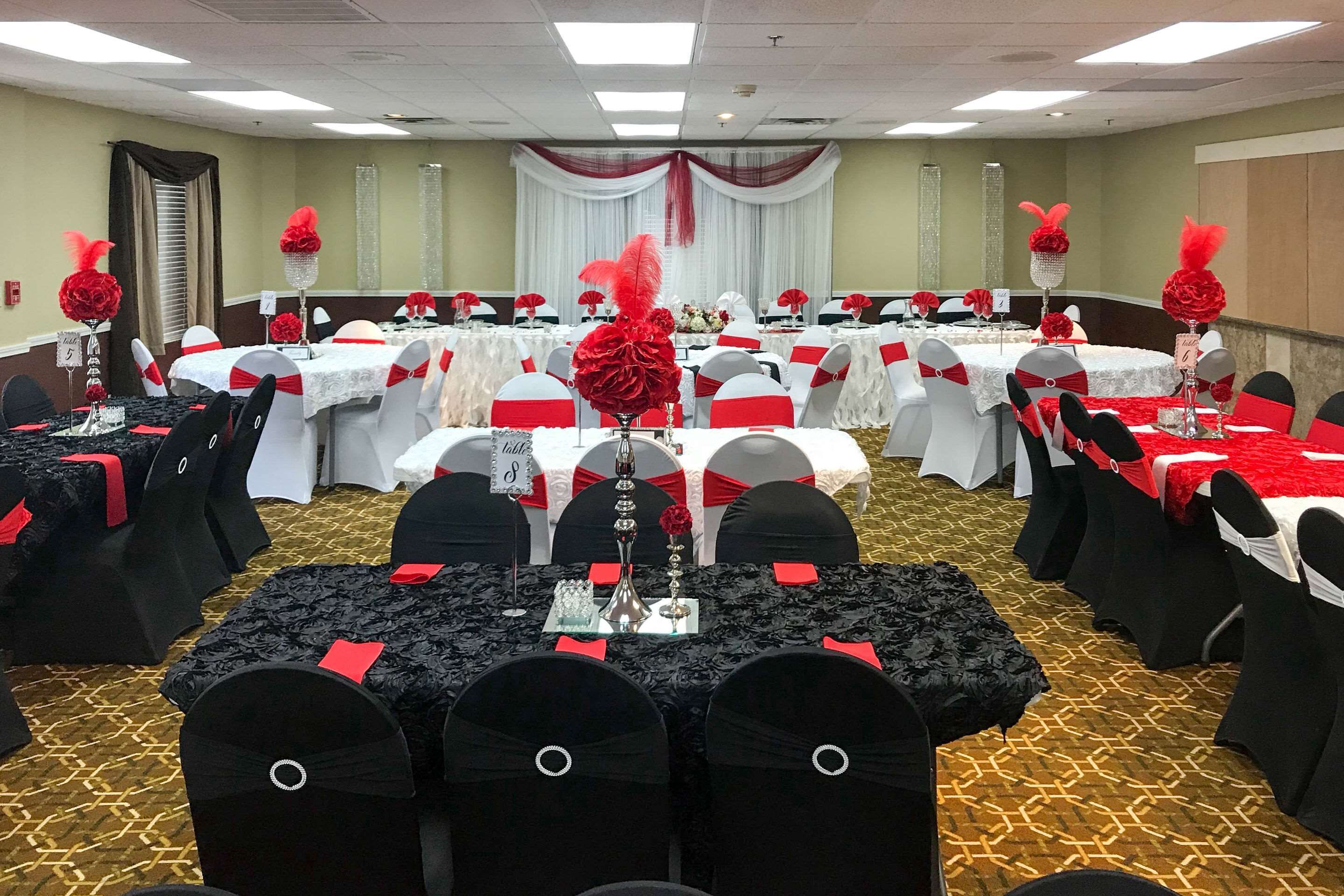 A banquet hall with round tables, black and white chairs, and red accents.