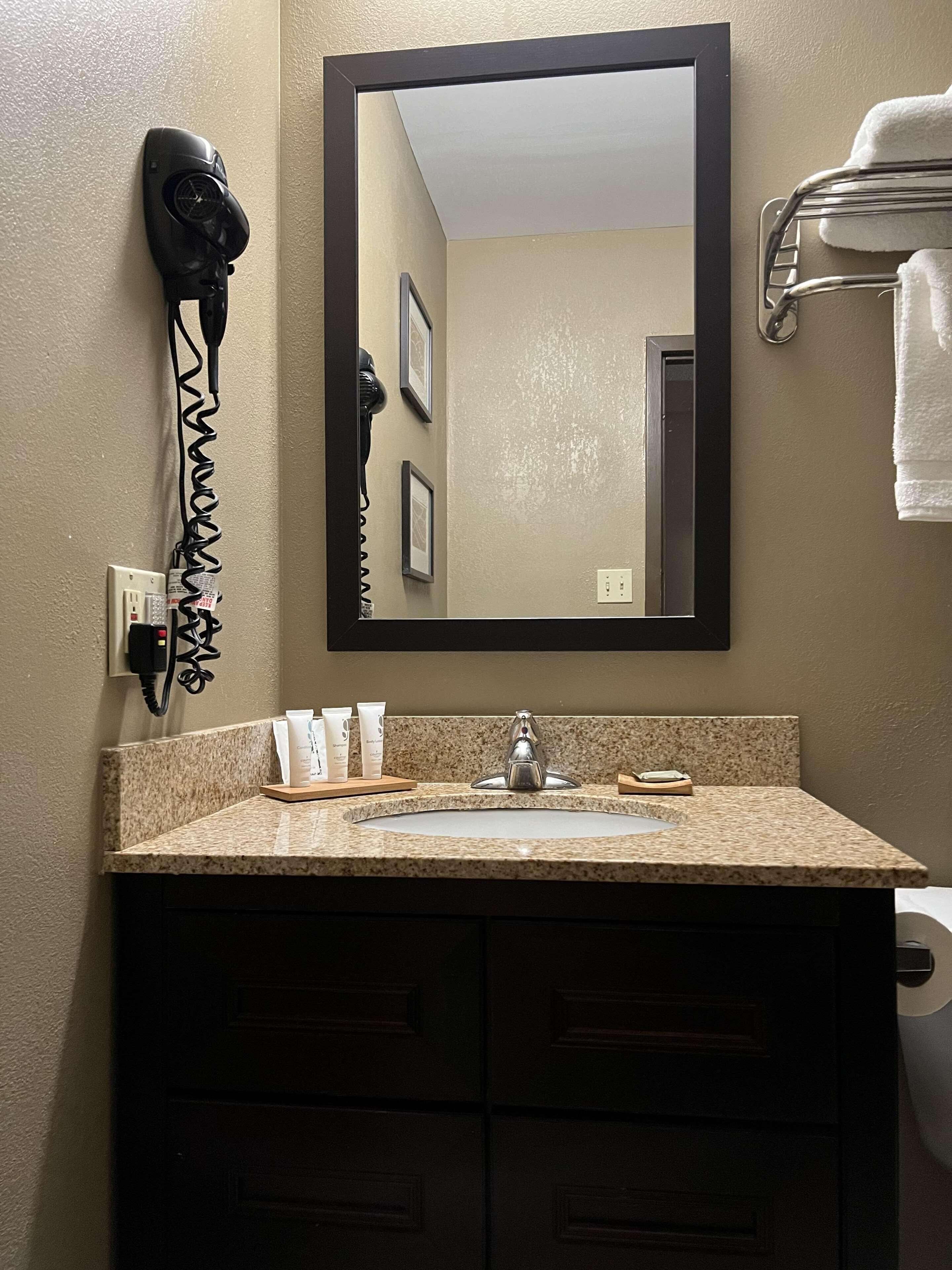A bathroom with a granite countertop, a sink, a mirror, a hairdryer, and a towel rack.