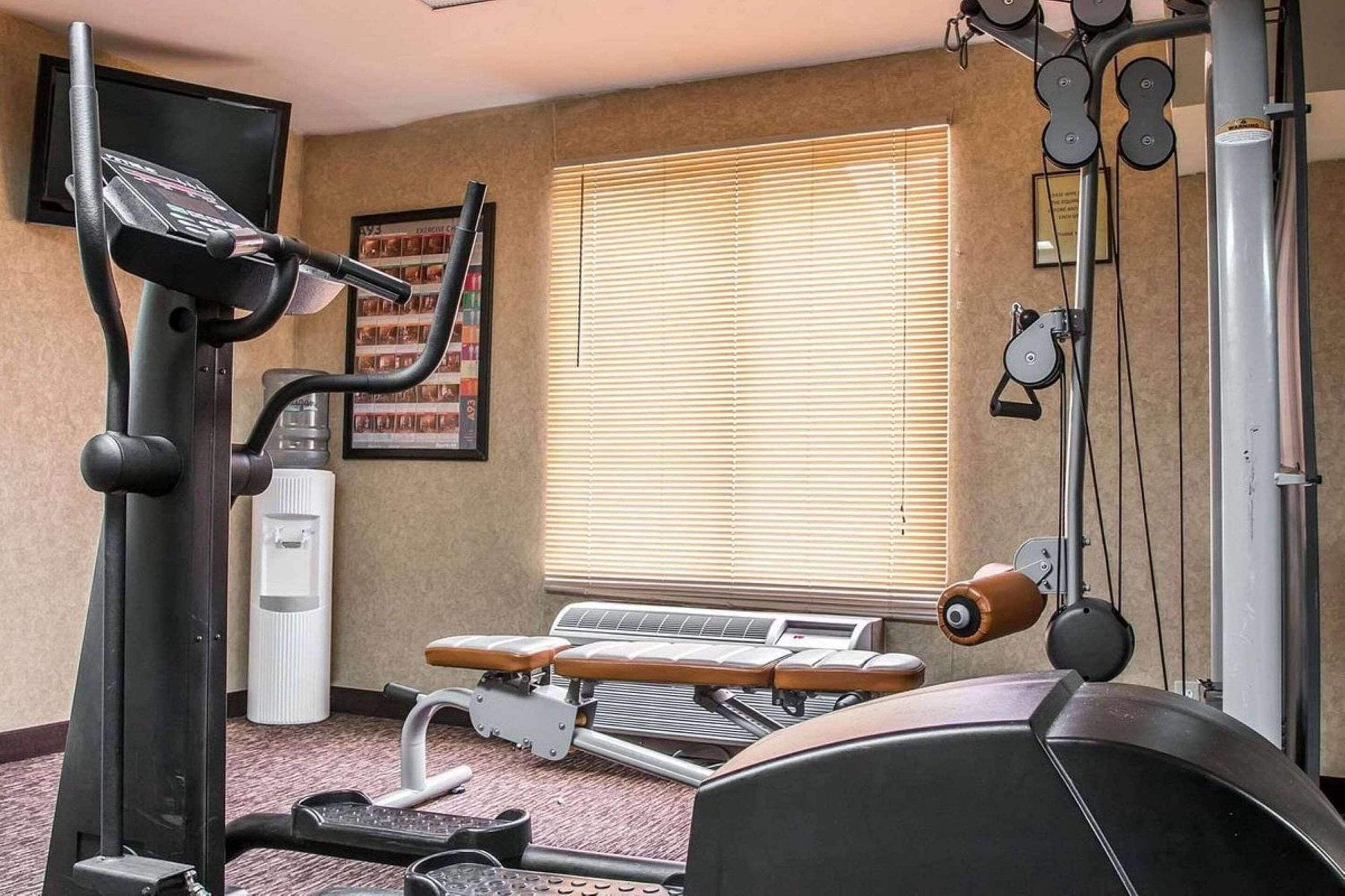 Uma academia com equipamentos de cardio, uma máquina de remo e uma televisão fixada na parede.