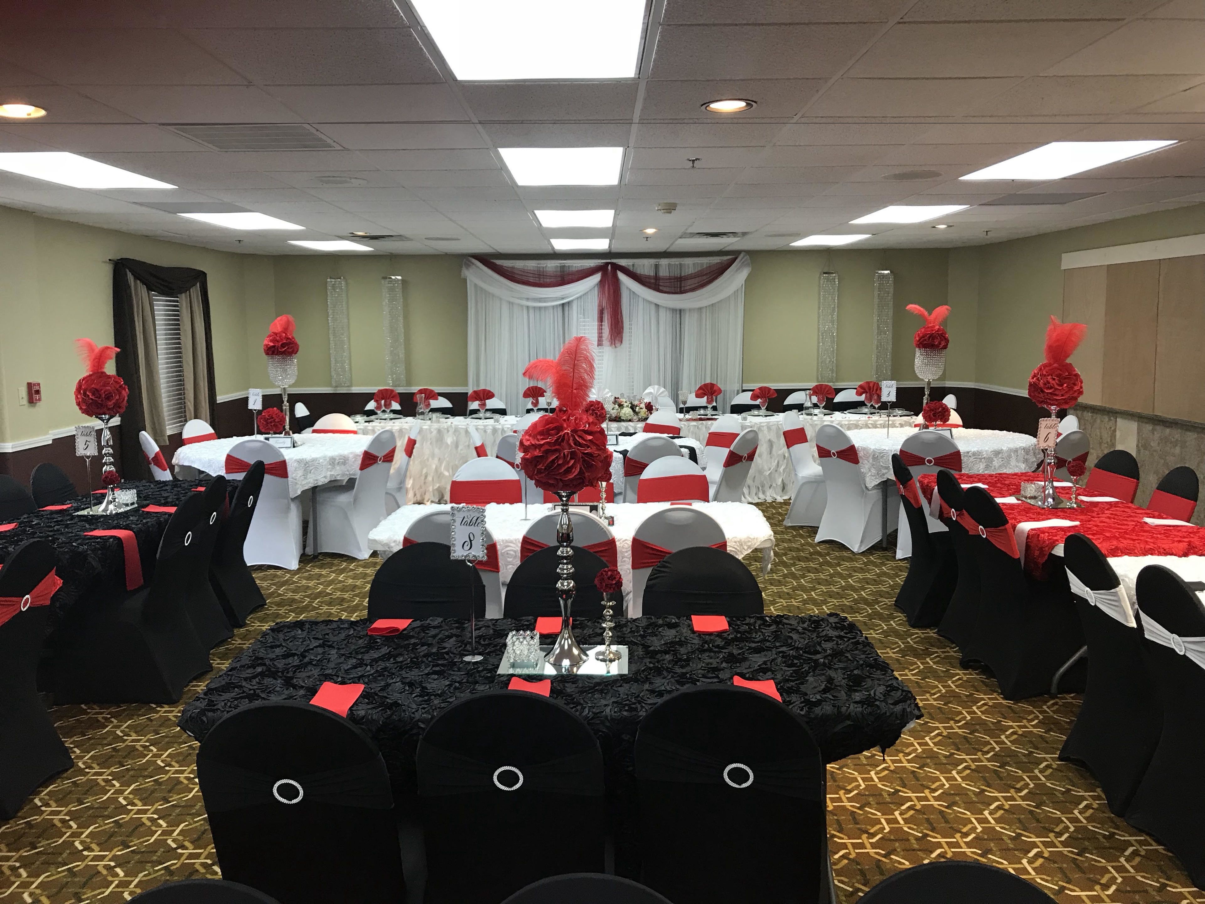 A banquet hall with round tables, black and white chairs, and red and white decorations.