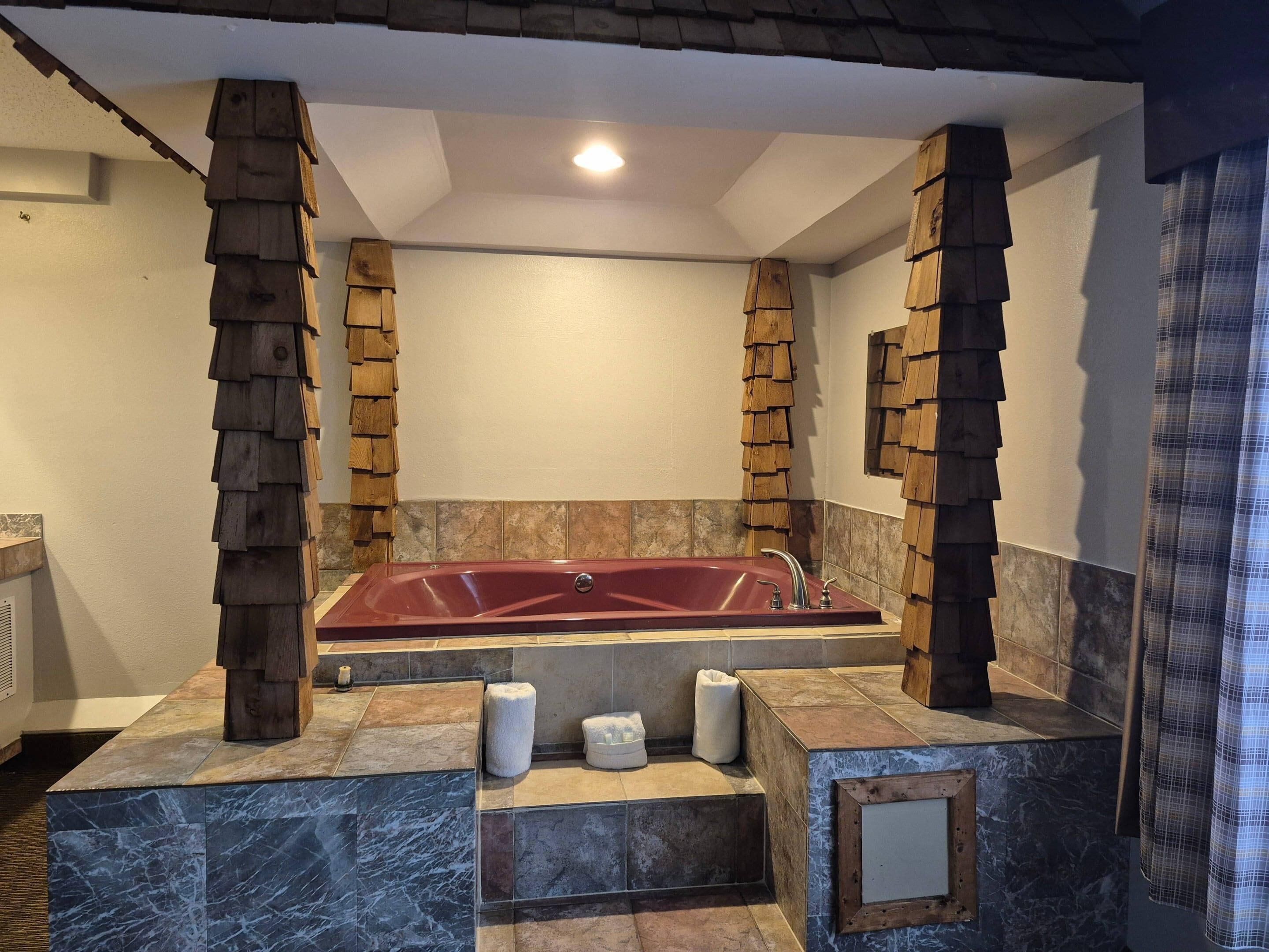 A bathroom with a large red bathtub, wooden pillars, and marble tiles.