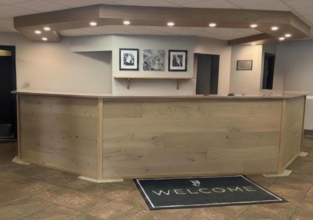 A reception desk with a 'WELCOME' mat, framed artwork on the wall, and a wooden finish.