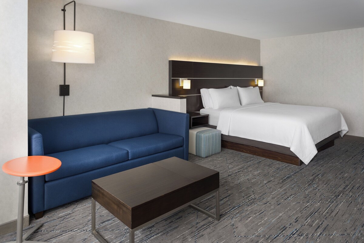 A hotel room with a bed, a blue sofa, a small table, and a nightstand with a lamp.