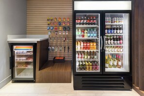 A vending machine with various beverages and snacks, a refrigerator stocked with drinks, and a display of packaged goods on the wall. - Holiday Inn Express & Suites Johnstown by IHG (Johnstown)