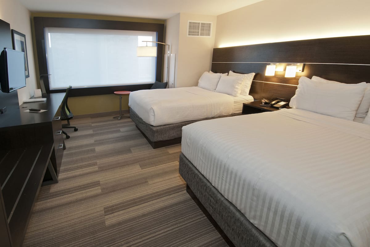 Habitación de hotel con dos camas, un escritorio, una silla, un televisor y una ventana con persianas.