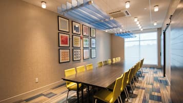 Une salle de conférence avec une longue table, des chaises jaunes et des œuvres d’art encadrées accrochées au mur.