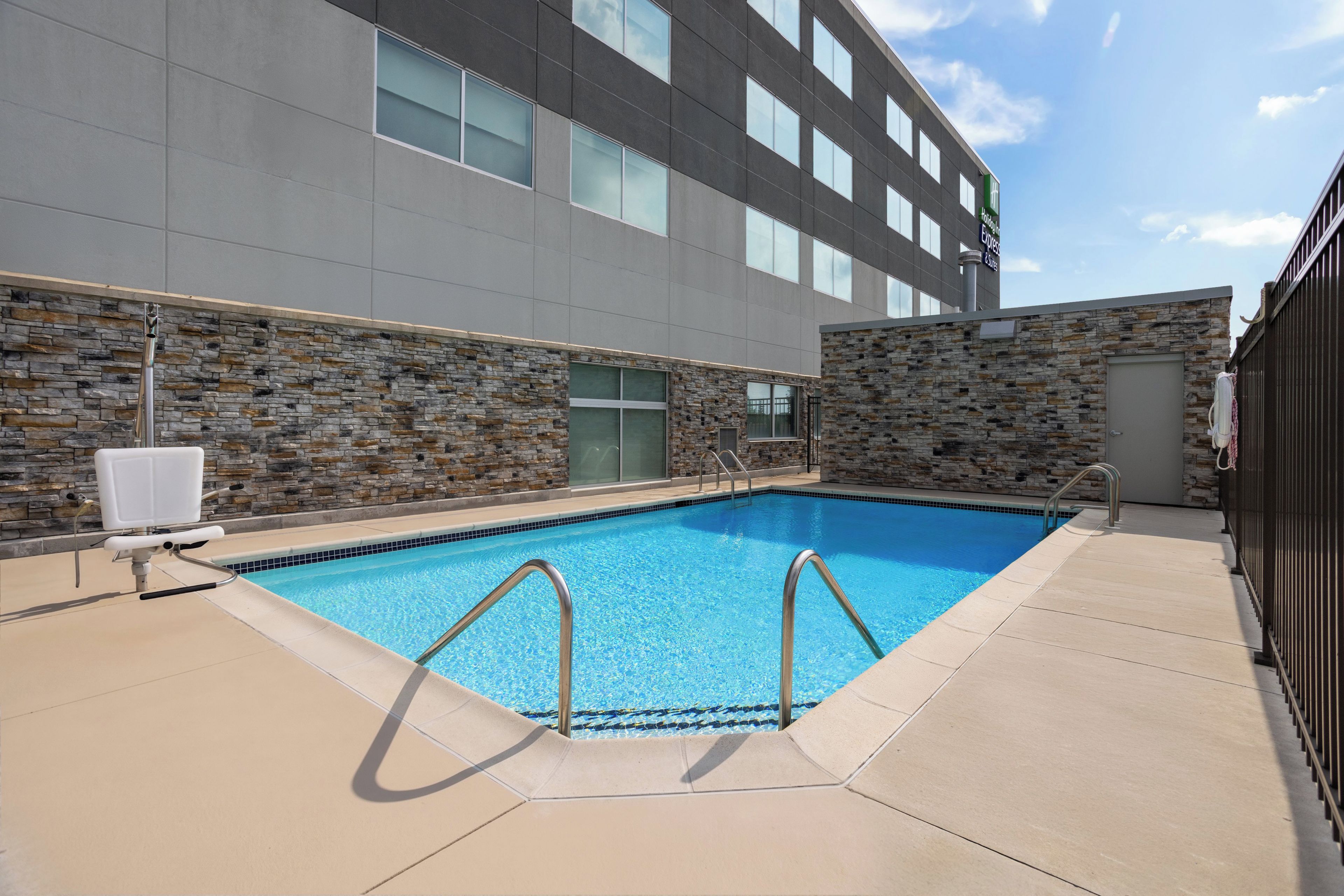A swimming pool with a stone wall and a modern building in the background.
