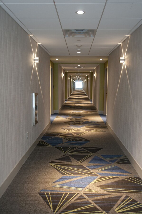 A long, narrow hotel corridor with patterned carpet, recessed lighting, and a mirrored wall on one side. - Holiday Inn Express & Suites Johnstown by IHG (Johnstown)