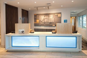 A reception desk with a modern design, featuring a check-in/out sign, a digital display, and a mounted security camera. - Holiday Inn Express & Suites Johnstown by IHG (Johnstown)