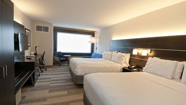 A hotel room with two beds, a desk, a chair, a TV, and a window.