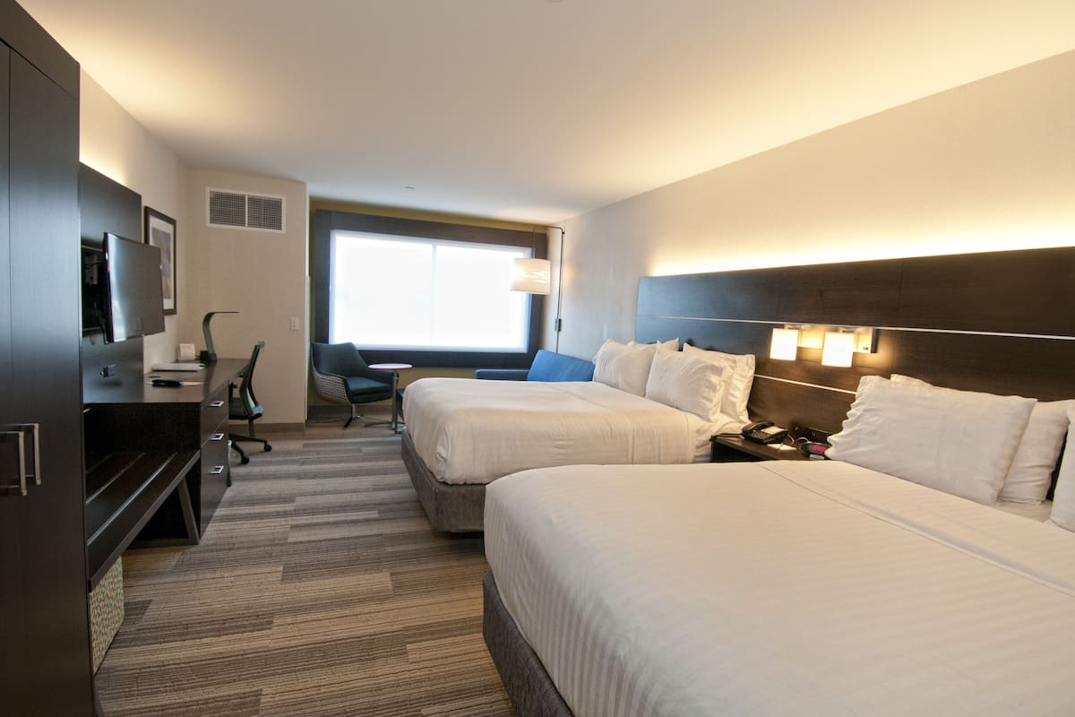 Una habitación de hotel con dos camas, un escritorio, una silla, un televisor y una ventana.