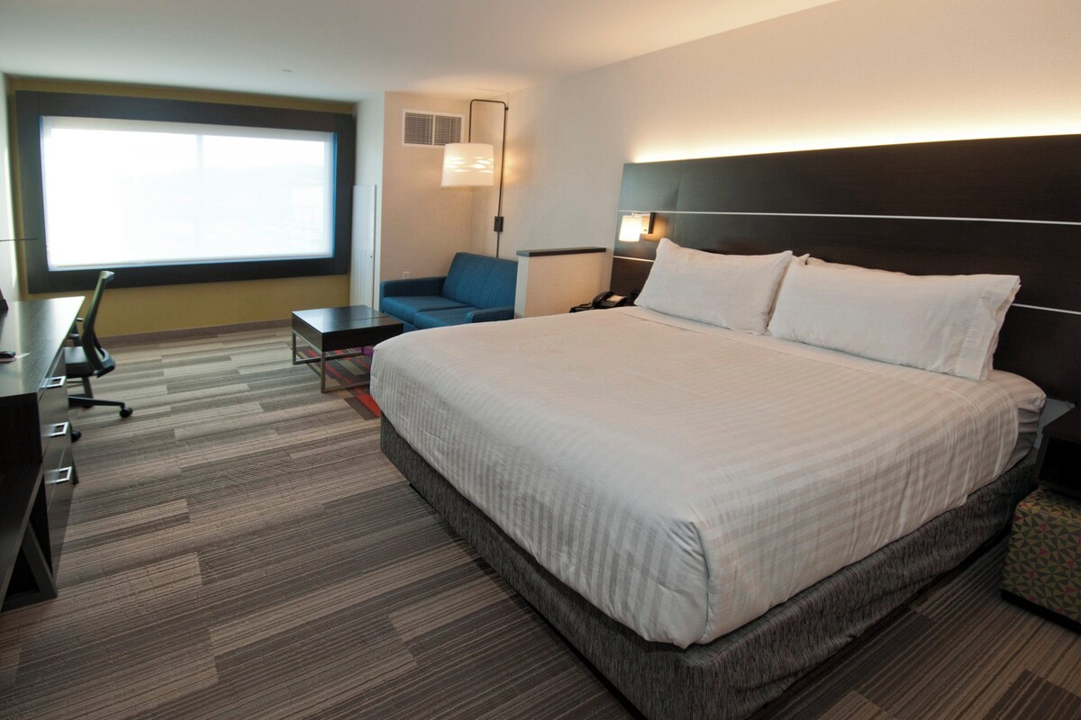 A hotel room with a large bed, a desk with a chair, a sofa, and a large window.