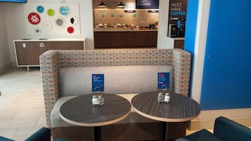 A seating area with two round tables, a wall-mounted TV, and a coffee station.