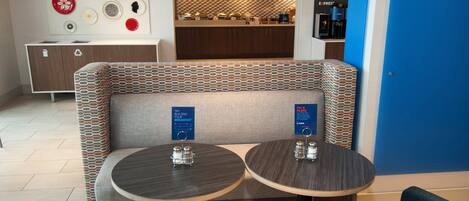 A seating area with two round tables, a wall-mounted TV, and a coffee station.