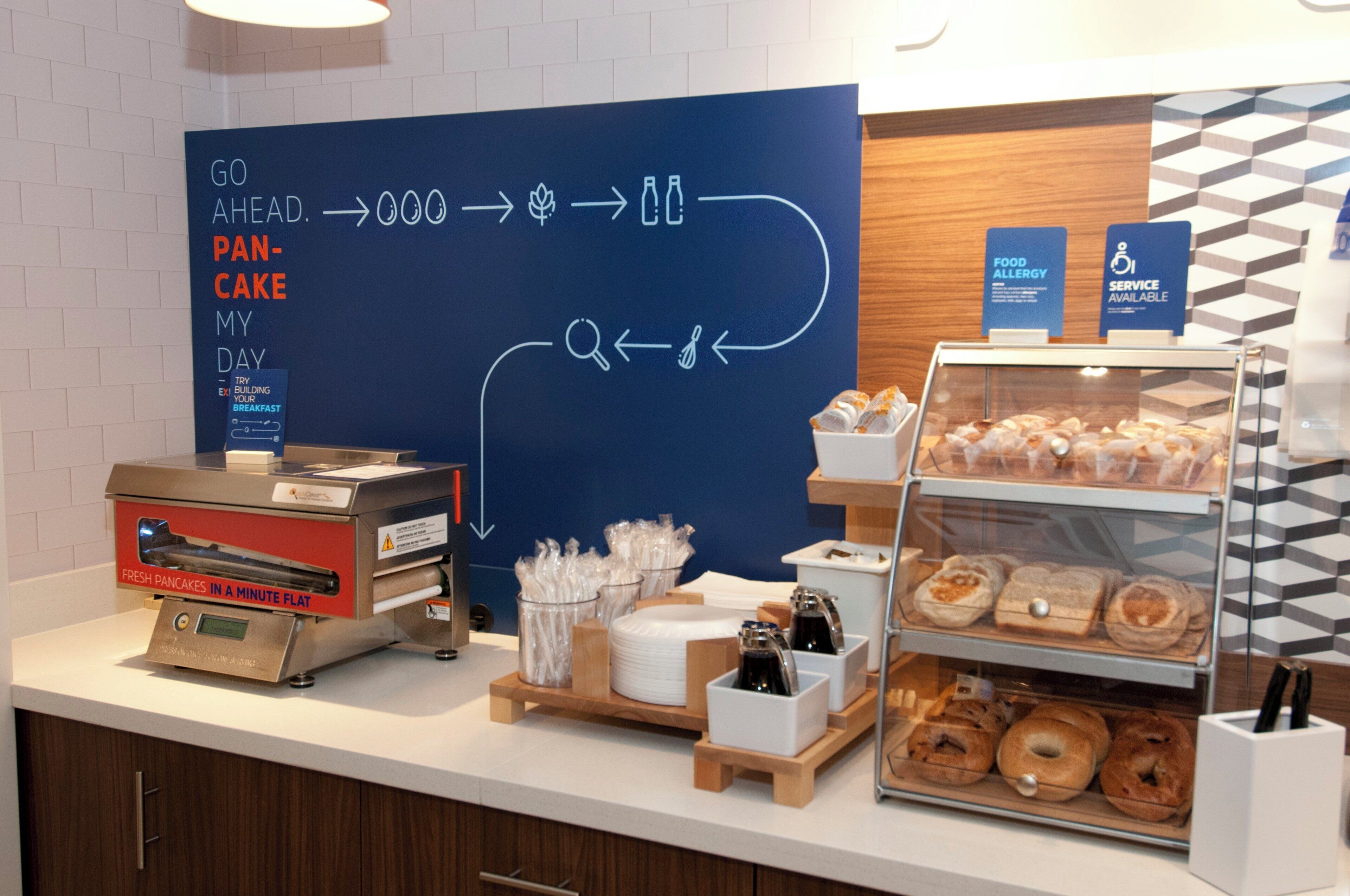 A breakfast counter with a flat-screen TV displaying a menu, a coffee machine, and a display case with pastries.