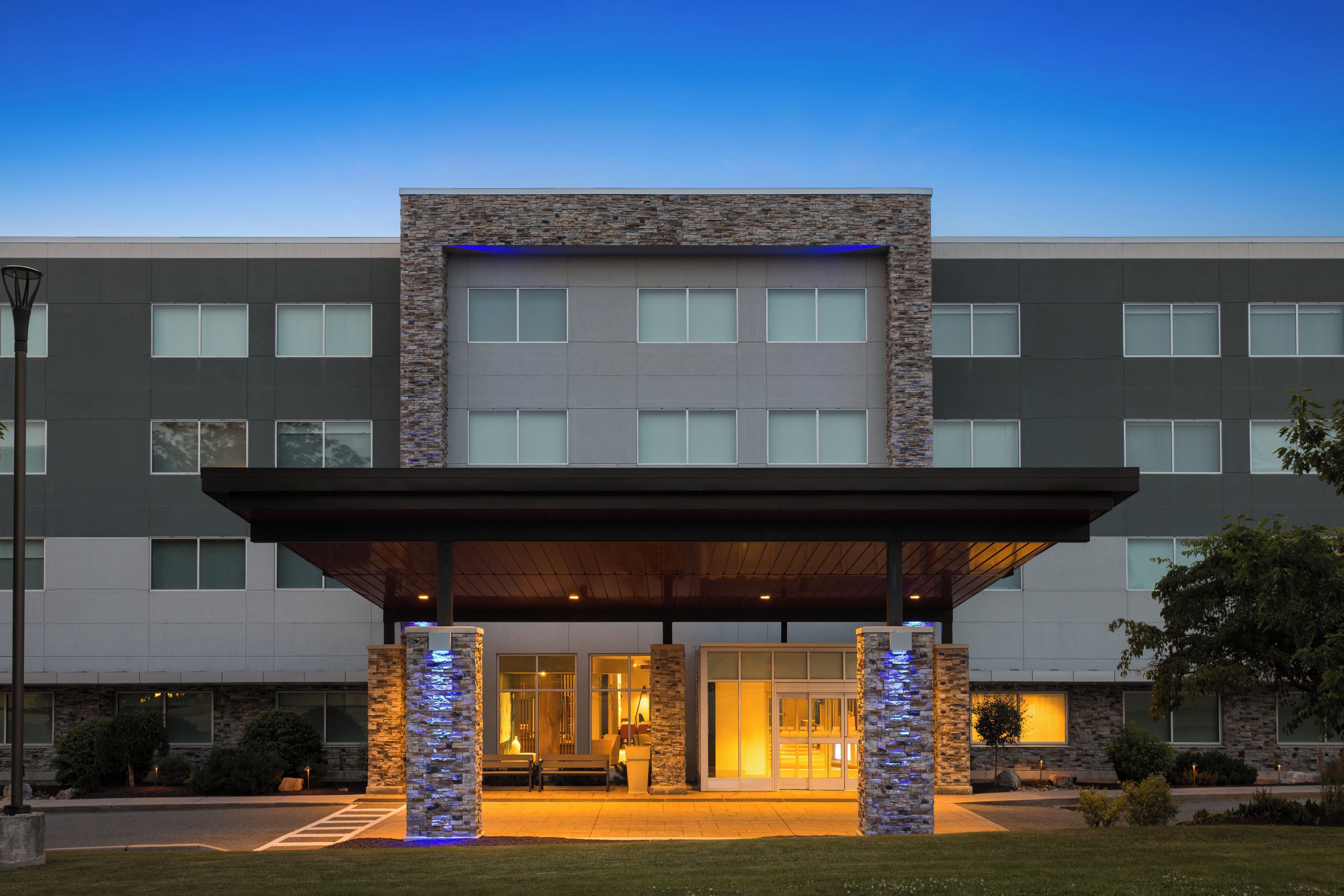 A modern hotel entrance with a covered walkway, stone facade, and large windows.